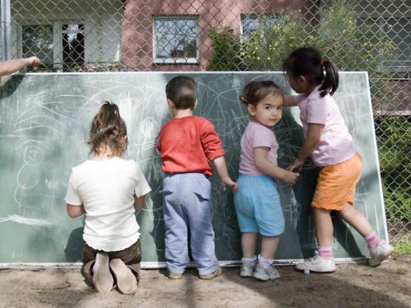 Fünf Kinder in einer Kita im Garten malen an einer Tafel.