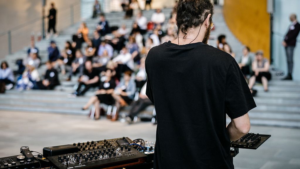 Ein DJ am Pult vor dem Publikum, das auf den Stufen der Suedtreppe sitzt